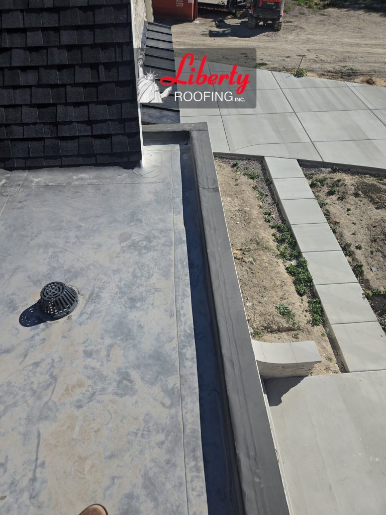 TPO roof membrane with a drain strainer and perimeter edge beside a shingle roof section in American Fork